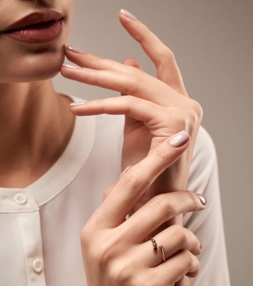 Close up portrait of incognito female model presenting silver ring with black and white stones. Crop of woman posing in studio, isolated on grey background. Concept of expensive jewelry.